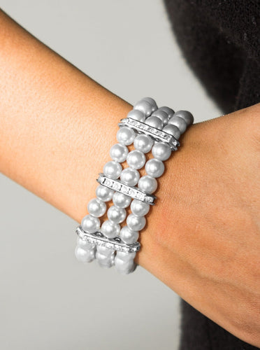 Classic silver pearls are threaded along elastic stretchy bands, creating colorful layers across the wrist. Encrusted in glittery white rhinestones, shimmery silver frames fit around the pearl strands, joining the bracelets.  Sold as one individual bracelet.  