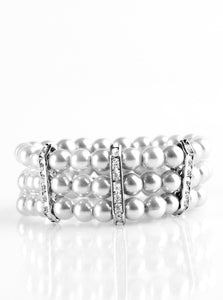 Classic silver pearls are threaded along elastic stretchy bands, creating colorful layers across the wrist. Encrusted in glittery white rhinestones, shimmery silver frames fit around the pearl strands, joining the bracelets.  Sold as one individual bracelet.