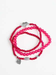 An array of glassy and polished pink beads are threaded along stretchy bands. Infused with silver accents, a collection of silver heart charms and a bead spelling out the word, "love", adorn the beaded strands for a romantic finish.  Sold as one set of three bracelets.