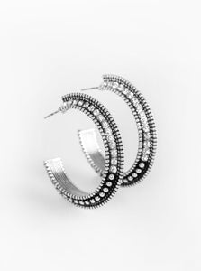 The top half of a bold silver frame is encrusted in glassy white rhinestones, giving way to glistening silver studs for an edgy finish. Earring attaches to a standard post fitting. Hoop measures approximately 1 1/4" in diameter.  Sold as one pair of hoop earrings.
