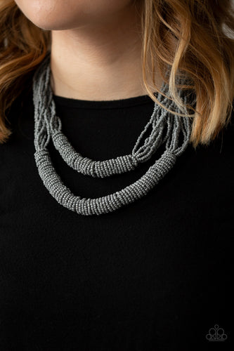 Countless layers of neutral gray seed beads drape below the collar. Additional strands of gray seed beads wrap around the center of the layers, creating two bulky rows for a seasonal flair. Features an adjustable clasp closure.  Sold as one individual necklace. Includes one pair of matching earrings.  Always nickel and lead free.