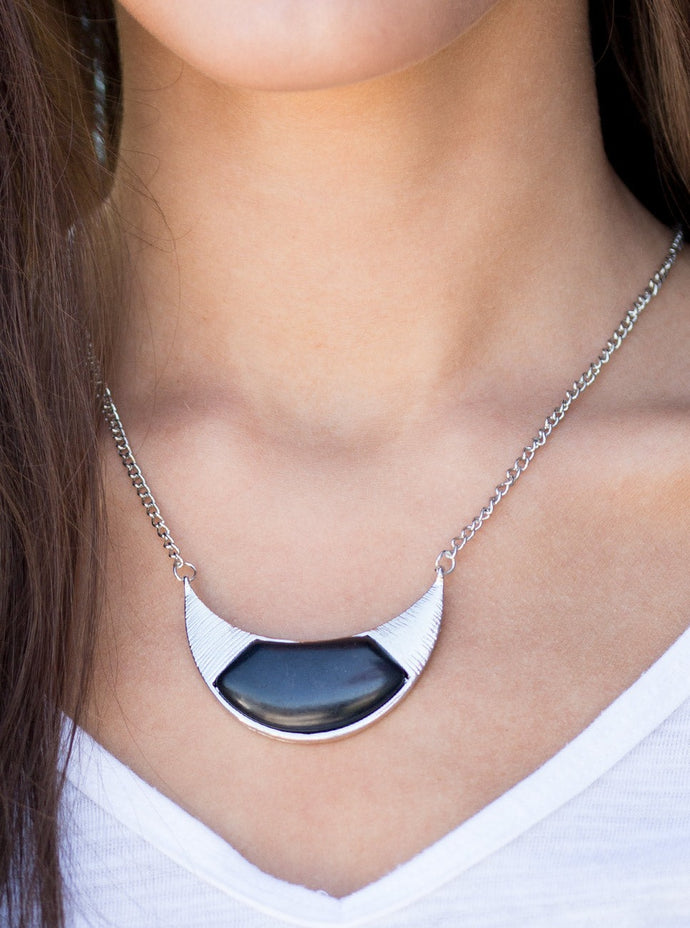 A smooth black stone is pressed into the center of a crescent-shaped frame, creating a tribal inspired pendant below the collar. The glistening silver frame is delicately scratched in shimmer for a handcrafted, artisanal finish. Features an adjustable clasp closure.  Sold as one individual necklace. Includes one pair of matching earrings.  