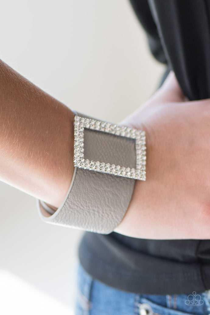 Two rows of dazzling white rhinestones coalesce into a rectangular frame. The glittery frame is threaded along a band of gray leather, creating a stunning centerpiece. Features an adjustable snap closure.  Sold as one individual bracelet.   Always nickel and lead free.