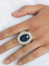 Load image into Gallery viewer, An over sized oval blue gem is pressed into the center of a round silver frame encrusted in mismatched white rhinestones for a glamorous look. Features a stretchy band for a flexible fit.  Featured inside The Preview at ONE Life!   Sold as one individual ring.   