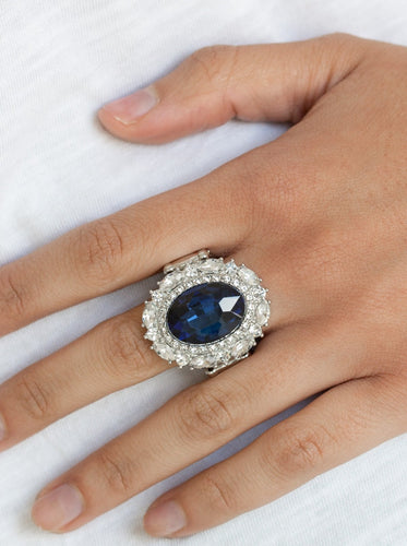 An over sized oval blue gem is pressed into the center of a round silver frame encrusted in mismatched white rhinestones for a glamorous look. Features a stretchy band for a flexible fit.  Featured inside The Preview at ONE Life!   Sold as one individual ring.   