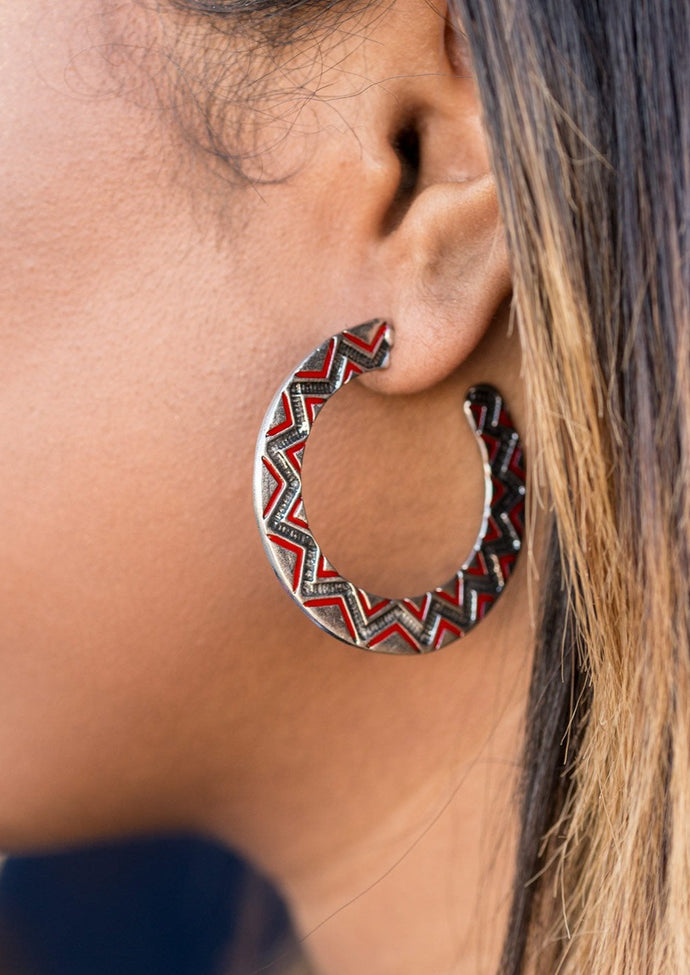A silver ribbon is etched in a radiant sunburst pattern. Highlighted with fiery red accents, the shimmery display falls from the ear in a trendy tribal fashion. Earring attaches to a standard post fitting. Hoop measures 1 5/8” in diameter.  Sold as one pair of hoop earrings.