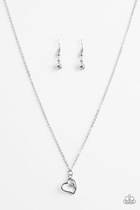 A solitaire white rhinestone sits off center inside of a silver heart frame, creating a timeless pendant below the collar. Features an adjustable clasp closure.  Sold as one individual necklace. Includes one pair of matching earrings.