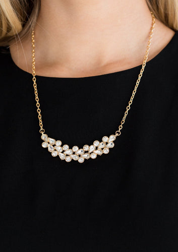 A collection of round and teardrop white rhinestones coalesce into a bowing gold pendant below the collar for a refined look. Features an adjustable clasp closure.  Sold as one individual necklace. Includes one pair of matching earrings.  