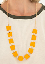 Load image into Gallery viewer, Vibrant geometric squares painted in the spring Pantone® of Marigold flare out along a long gold chain as it drapes along the chest. Sleek gold cylinders separate the square plates, adding warm metallic accents to the piece. Features an adjustable clasp closure.