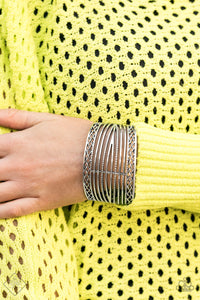 Bordered in crisscrossed details, hammering and smooth silver bars wrap back and forth across the wrist, coalescing into a thick silver cuff.