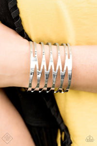 Brushed in a high-sheen finish, flat silver bars race back and forth across the wrist, coalescing into an edgy cuff decorated in sharp angles and dramatic patterns.