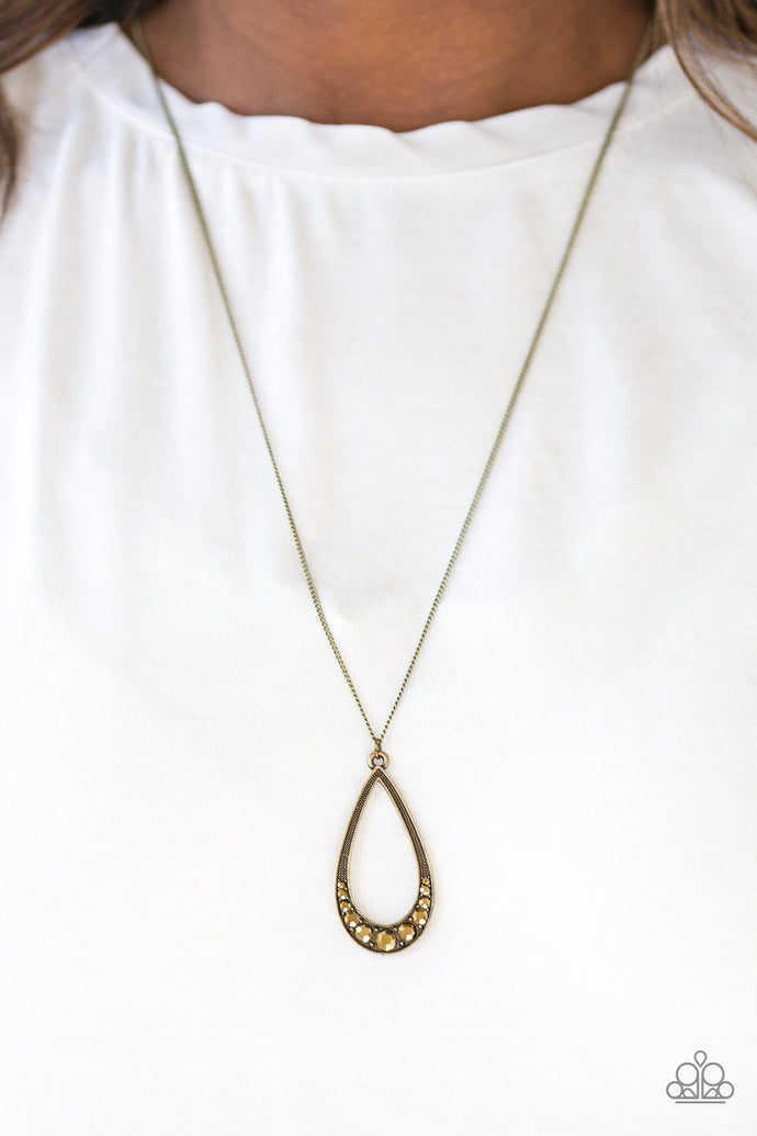Swinging from the bottom of an elongated brass chain, the bottom of a glistening brass teardrop is encrusted in glittery aurum rhinestones, creating a refined pendant. Features an adjustable clasp closure.  Sold as one individual necklace. Include one pair of matching earrings.  Always nickel and lead free.