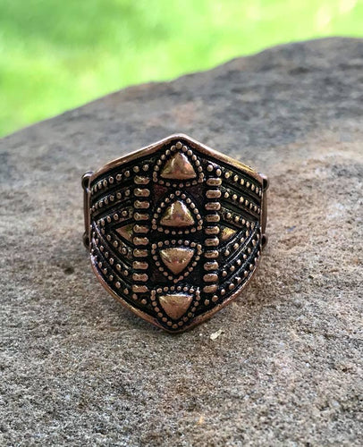 Brushed in an antiqued shimmer, dainty triangular frames are pressed down the center of a shimmery copper frame radiating with studded textures for a tribal inspired look. Features a stretchy band for a flexible fit.  Sold as one individual ring.