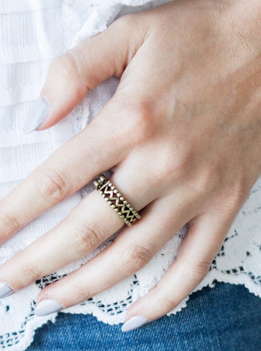 A shimmery brass bar zigzags down the center of a studded band for a tribal inspired look. Features a dainty stretchy band for a flexible fit.  Sold as one individual ring.