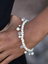 Load image into Gallery viewer, Classic white pearls are threaded along an elastic stretchy band. Etched in glistening textures, shimmery silver discs, pearl accents, and glittery crystal-like beading swing from the wrist, adding a refined twist to the timeless pearl palette.  Sold as one individual bracelet.