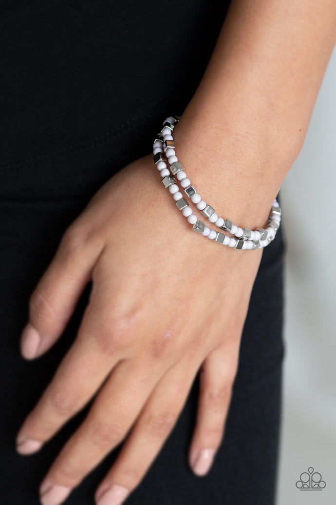 A collection of dainty gray beads and silver cube beads are threaded along stretchy bands around the wrist, creating colorful layers.  Sold as one set of two bracelets.  Always nickel and lead free