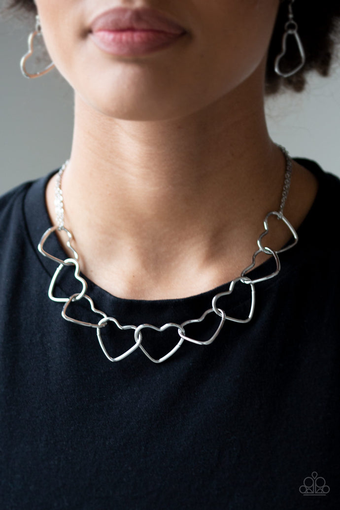Airy silver heart silhouettes connect below the collar for a flirtatious look. Features an adjustable clasp closure.  Sold as one individual necklace. Includes one pair of matching earrings.  Always nickel and lead free.