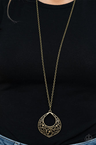 Brushed in an antiqued finish, studded brass vine-like filigree collects inside an abstract teardrop frame at the bottom of a lengthened brass chain for a whimsically rustic look. Features an adjustable clasp closure.  Sold as one individual necklace. Includes one pair of matching earrings.  Always nickel and lead free.