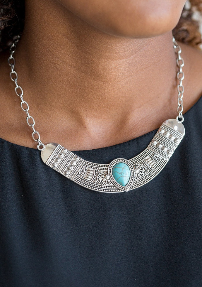 Embossed in floral and tribal inspired patterns, a shimmery silver crescent shaped frame swings below the collar in a fierce fashion. Chiseled into a tranquil teardrop, a refreshing turquoise stone is pressed into the center of the dramatic pendant for a seasonal finish. Features an adjustable clasp closure.  Sold as one individual necklace. Includes one pair of matching earrings. 