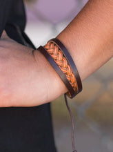Load image into Gallery viewer, Shiny brown and orange twine weave across the wrist, creating a colorful braid. Two strands of brown leather join the colorful braid, adding earthy accents to the urban layers. Features an adjustable sliding knot closure.  Sold as one individual bracelet.  