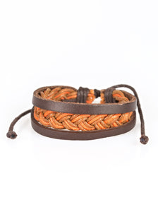 Shiny brown and orange twine weave across the wrist, creating a colorful braid. Two strands of brown leather join the colorful braid, adding earthy accents to the urban layers. Features an adjustable sliding knot closure. Sold as one individual bracelet.