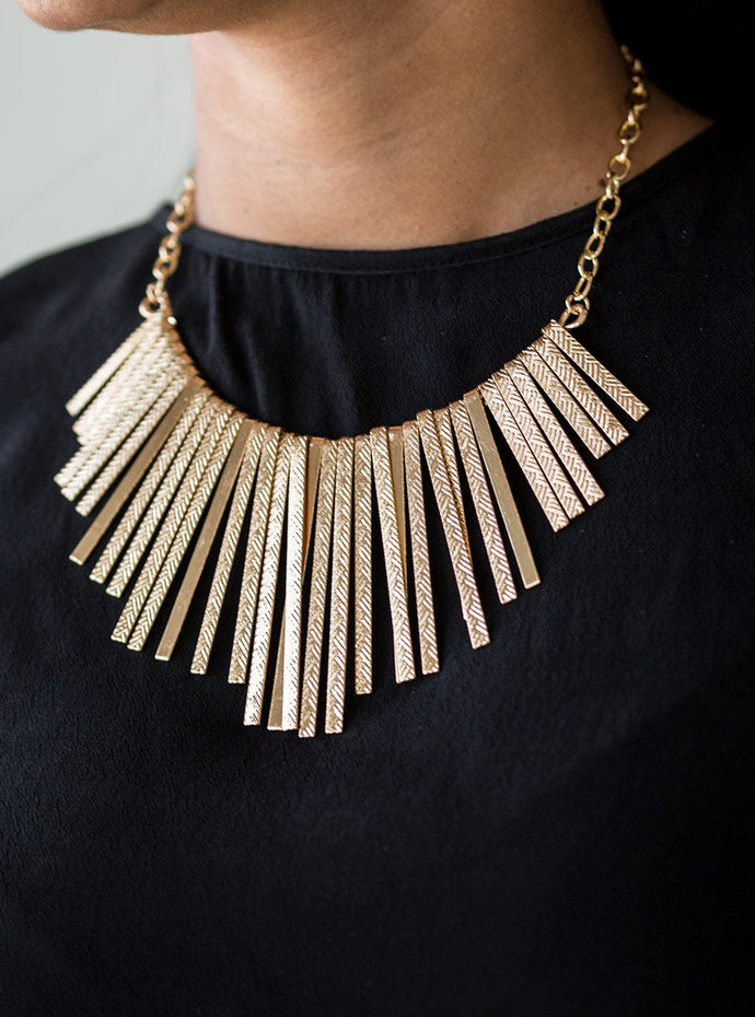 Embossed in edgy linear patterns, flat gold rods alternate with plain gold rods below the collar, creating a fiercely tapered fringe. Features an adjustable clasp closure.  Sold as one individual necklace. Includes one pair of matching earrings. 