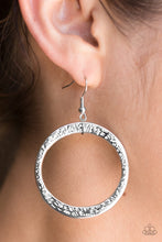 Load image into Gallery viewer, Delicately hammered in light-catching detail, an asymmetrical silver hoop swings from the ear for an artisan inspired look. Earring attaches to a standard fishhook fitting.  Sold as one pair of earrings.  Always nickel and lead free.