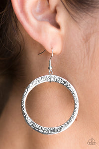 Delicately hammered in light-catching detail, an asymmetrical silver hoop swings from the ear for an artisan inspired look. Earring attaches to a standard fishhook fitting.  Sold as one pair of earrings.  Always nickel and lead free.