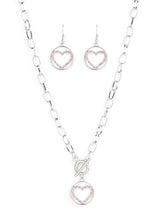 Load image into Gallery viewer, A pink rhinestone encrusted silver heart is nestled inside a shiny silver hoop, creating a charming pendant at the bottom of an exaggerated silver chain. Features a toggle closure.  Sold as one individual necklace. Includes one pair of matching earrings.