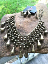 Load image into Gallery viewer, Threaded along metallic rods, stacked brass beads give way to shimmery teardrops. The edgy fringe flawlessly drapes beneath the collar, creating a sassy tapered fringe. Features an adjustable clasp closure.  Sold as one individual necklace. Includes one pair of matching earrings.