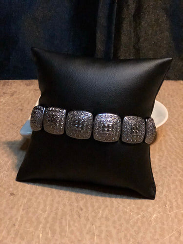 Brushed in an antiqued shimmer, textured silver frames are threaded along stretchy elastic bands, linking around the wrist for a tribal inspired look.  Sold as one individual bracelet.